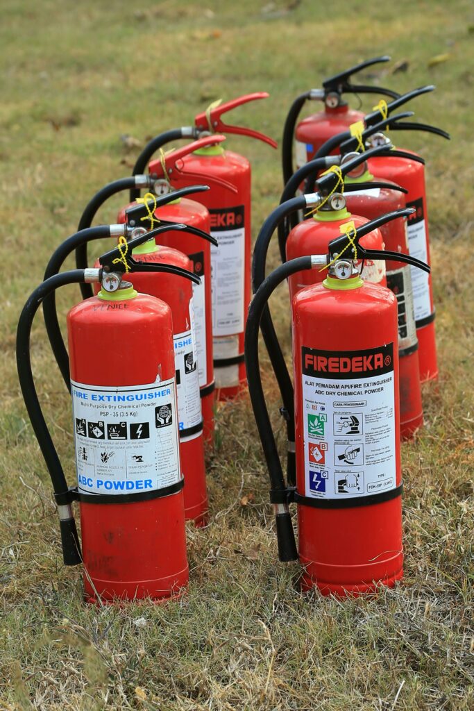 Multiple fire extinguishers lined up on grass, ready for emergency use, showcasing fire safety equipment.