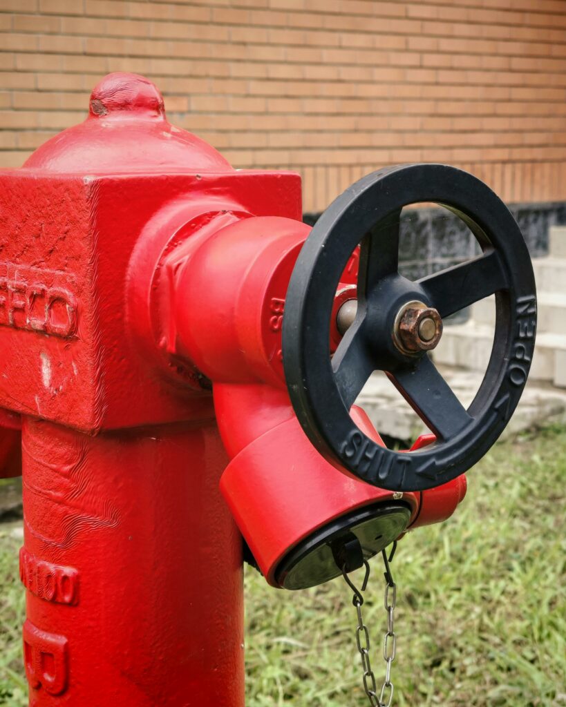 Close-up of a red fire hydrant with valve in an outdoor setting, suitable for safety and infrastructure themes.